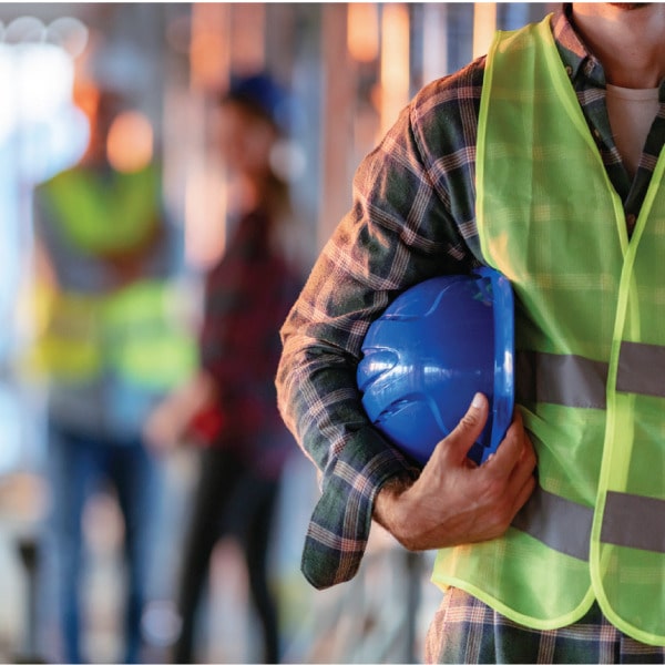 Construction worker in reflective vest holding a hard hat on a job site, representing operations and compliance.