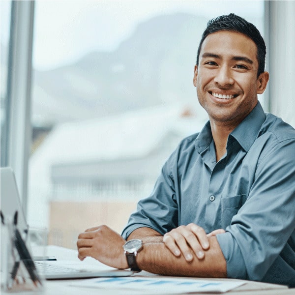 Man smiling at his desk in a bright office setting, conveying confidence, approachability, and expert consulting support